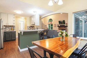Eine moderne Küche mit Kochinsel, Essbereich mit Holztisch und ein Wohnzimmer mit Kamin.