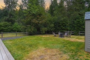 Ein Garten mit einer Holzterrasse, einem Grill und einem von Bäumen gesäumten, eingezäunten Bereich.