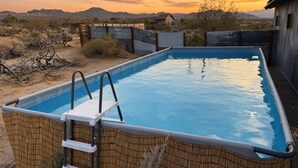 Una piscina rectangular con escalera, rodeada por una cerca de madera, ubicada en un paisaje desértico con montañas al fondo.