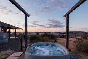 A hot tub with a view of a desert landscape, a covered outdoor area, and a building with a modern design. - Park-edge hot tub retreat · dogs welcome (Joshua Tree)