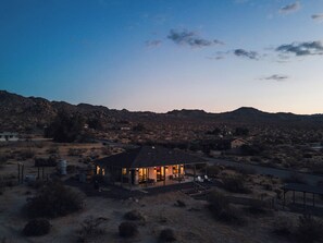 A single-story house with a covered patio, surrounded by a dry, hilly landscape. - Park-edge hot tub retreat · dogs welcome (Joshua Tree)
