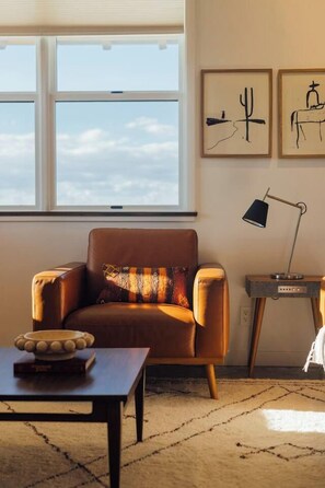 A room with a leather armchair, a small table with a bowl, a lamp on a side table, and a window with a view.