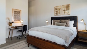 Un dormitorio con una cama de madera, un escritorio con silla y dos lámparas de noche.