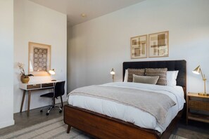 Un dormitorio con una cama de madera, un escritorio con silla y dos lámparas de noche.