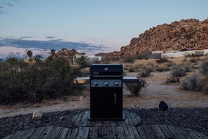 A barbecue grill on a wooden deck with a rocky landscape and sparse vegetation in the background. - Park-edge hot tub retreat · dogs welcome (Joshua Tree)