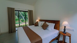 A hotel room with a large bed, two bedside lamps, a view of greenery outside, and a wooden headboard.