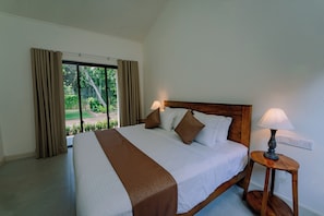 A hotel room with a large bed, two bedside lamps, a view of greenery outside, and a wooden headboard.