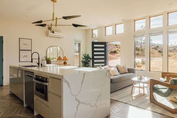A modern kitchen with a marble island, built-in appliances, and a large window overlooking a desert landscape. - Casa Mariposa| 5 Minutes to Park Entrance| Hot Tub (Joshua Tree)