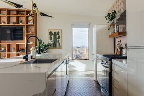 A modern kitchen with a large island, built-in appliances, and a view to the outdoors. - Casa Mariposa| 5 Minutes to Park Entrance| Hot Tub (Joshua Tree)