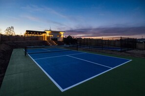 Cancha de tenis a l'aire lliure amb xarxa, envoltada per una tanca i un edifici amb escales que hi menen.