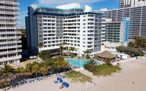 A multi-story hotel with a pool area, palm trees, and beach chairs. - Lovely Beachfront Condo w/Balcony overlooking the Atlantic Ocean (Fort Lauderdale)