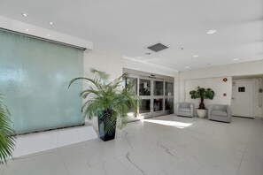 A spacious lobby with a large window, a reception desk, a potted plant, and a fire alarm.