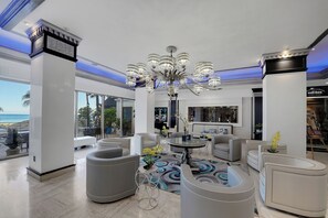 A modern living room with a large chandelier, comfortable seating, and a view of the ocean.