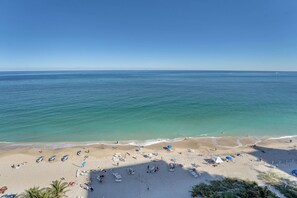 Una playa con cielos despejados, aguas tranquilas y una orilla arenosa con tumbonas y sombrillas.