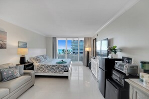 A modern hotel room with a bed, a sofa, a kitchenette, and a balcony with a view of the sea. - Lovely Beachfront Condo w/Balcony overlooking the Atlantic Ocean (Fort Lauderdale)