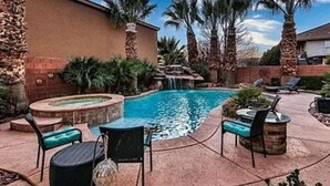 A swimming pool with a waterfall feature, surrounded by palm trees and outdoor seating. - Little Valley Oasis Resort Pool & Palm Paradise (St. George)