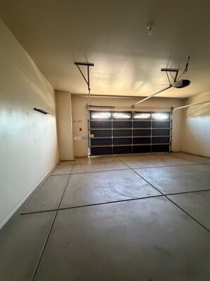 Un garage avec un sol carrelé, une porte de garage fermée et des luminaires suspendus au plafond.