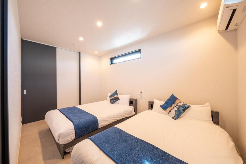 A hotel room with two beds, a window, and an air conditioning unit.