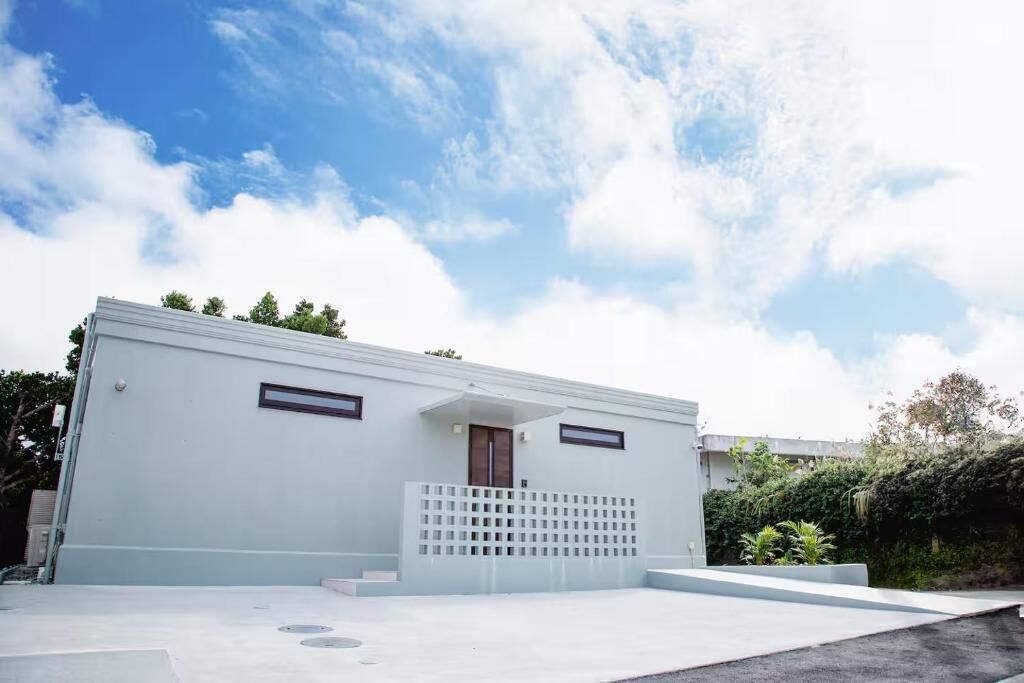 A modern building with a flat roof, a small entrance, and a white exterior.