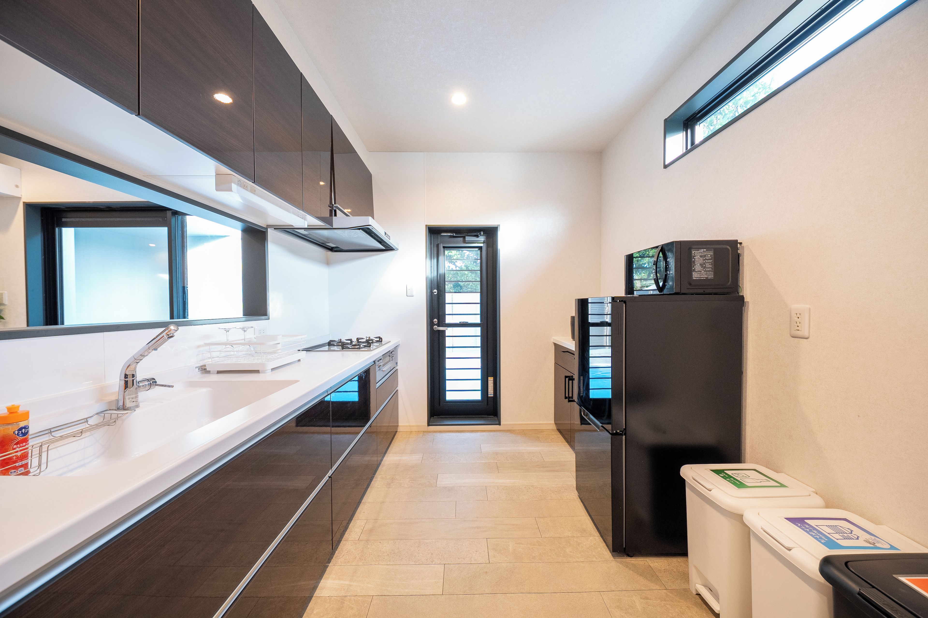 A modern kitchen with a stainless steel sink, a black refrigerator, and a microwave on top.