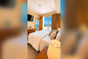 Ein Hotelzimmer mit Bett, Fernseher, Nachttisch und Meerblick.