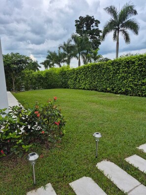 Un césped cuidado con setos, una palmera y un jardín lleno de flores rojas.