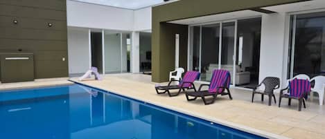 A modern outdoor pool area with lounge chairs and a covered patio.