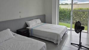 Una habitación de hotel con dos camas, una mesita de noche y un ventilador de pie.