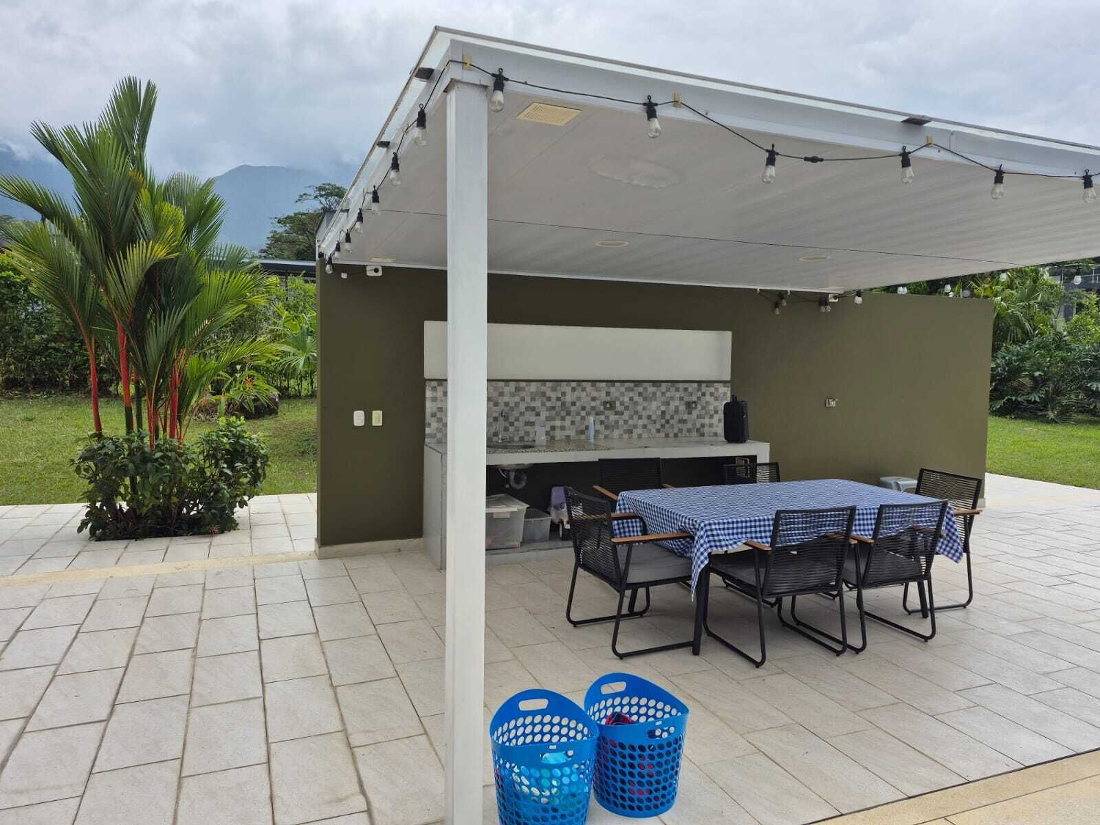 An outdoor patio with a covered barbecue area, a table with chairs, and two blue baskets.