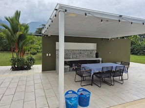Un patio exterior con una zona de barbacoa cubierta, una mesa con sillas y dos cestas azules.