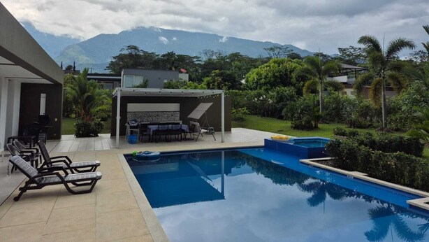 Un área de piscina moderna al aire libre con sillones de descanso, zona de barbacoa y vistas a montañas al fondo.