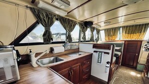 Cozinha compacta com pia, fogão e bancada pequena. Há uma janela com cortinas e vista para o exterior.