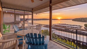 A balcony with a table and chairs, a ceiling fan, and a view of a sunset over a body of water. - Main Channel Views, 3 Heated Pools & Gated Resort (Lake Ozark)