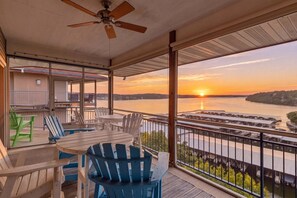 Ein Balkon mit Tisch und Stühlen, einem Deckenventilator und Blick auf einen Sonnenuntergang über dem Wasser.