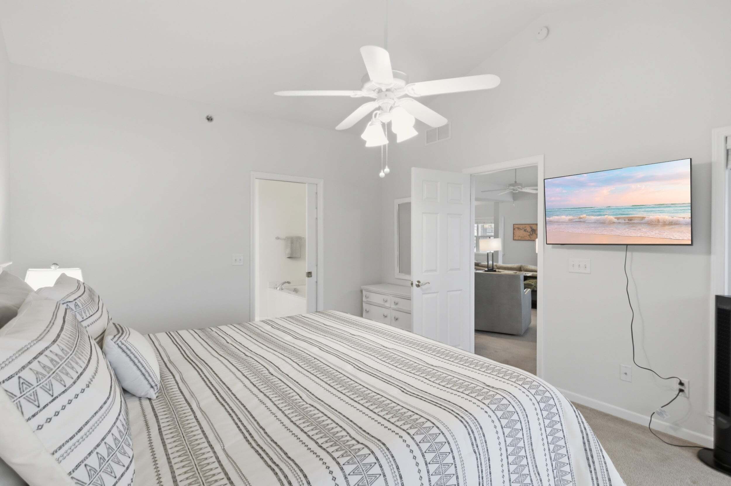 Une chambre à coucher avec un lit, un ventilateur de plafond, une télévision et une vue sur la cuisine.