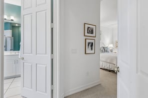 A hallway leading to a bedroom with a bed, a nightstand, and a lamp. There are two framed pictures on the wall. - San Remo - Hosted by Moore AI Rentals (Fernandina Beach)