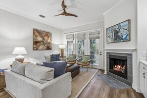 A living room with a fireplace, a ceiling fan, and a large abstract painting. - San Remo - Hosted by Moore AI Rentals (Fernandina Beach)