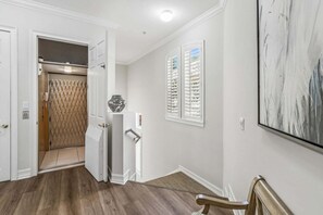 Um corredor com chão de madeira, uma porta que dá para um quarto, um radiador e um grande quadro abstrato na parede.