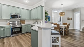 Een moderne keuken met inbouwapparatuur, een eethoek met een groot schiereiland, en een woonruimte met een eettafel en stoelen.