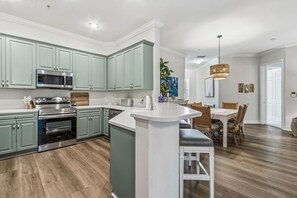 A modern kitchen with built-in appliances, a dining area with a large island, and a living space with a dining table and chairs. - San Remo - Hosted by Moore AI Rentals (Fernandina Beach)