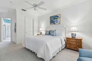 A bedroom with a bed, nightstands, a ceiling fan, a painting, and a door. - San Remo - Hosted by Moore AI Rentals (Fernandina Beach)