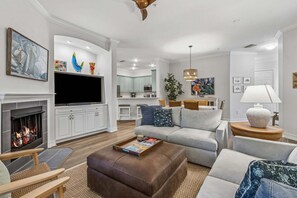 A modern living room with a fireplace, a television, and a dining area with a table and chairs. - San Remo - Hosted by Moore AI Rentals (Fernandina Beach)