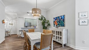 Een eetruimte met een witte tafel, rieten stoelen, een hanglamp en een kast met glazen deuren.