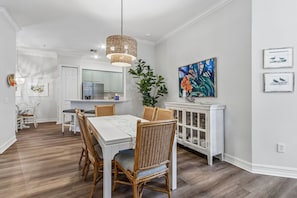 A dining area with a white table, wicker chairs, a hanging light fixture, and a cabinet with glass doors. - San Remo - Hosted by Moore AI Rentals (Fernandina Beach)