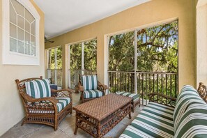 A sunlit patio with wicker furniture and large windows overlooking a wooded area. - San Remo - Hosted by Moore AI Rentals (Fernandina Beach)