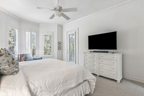 Quarto com uma cama grande, televisão em uma cômoda e ventilador de teto.