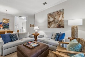 A modern living room with a sectional sofa, a coffee table, a side table, a lamp, and a large abstract painting on the wall. - San Remo - Hosted by Moore AI Rentals (Fernandina Beach)
