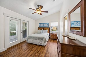 Ein Schlafzimmer mit Bett, Kommode, Spiegel, Deckenventilator und einem Fenster mit Jalousien.