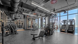 Et træningscenter med forskelligt træningsudstyr, store vinduer og et højt loft med synlige ventilationskanaler.