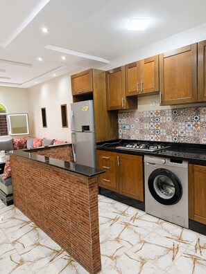Een moderne keuken met houten kastjes, een roestvrijstalen koelkast, een wasmachine en een betegelde spatwand.